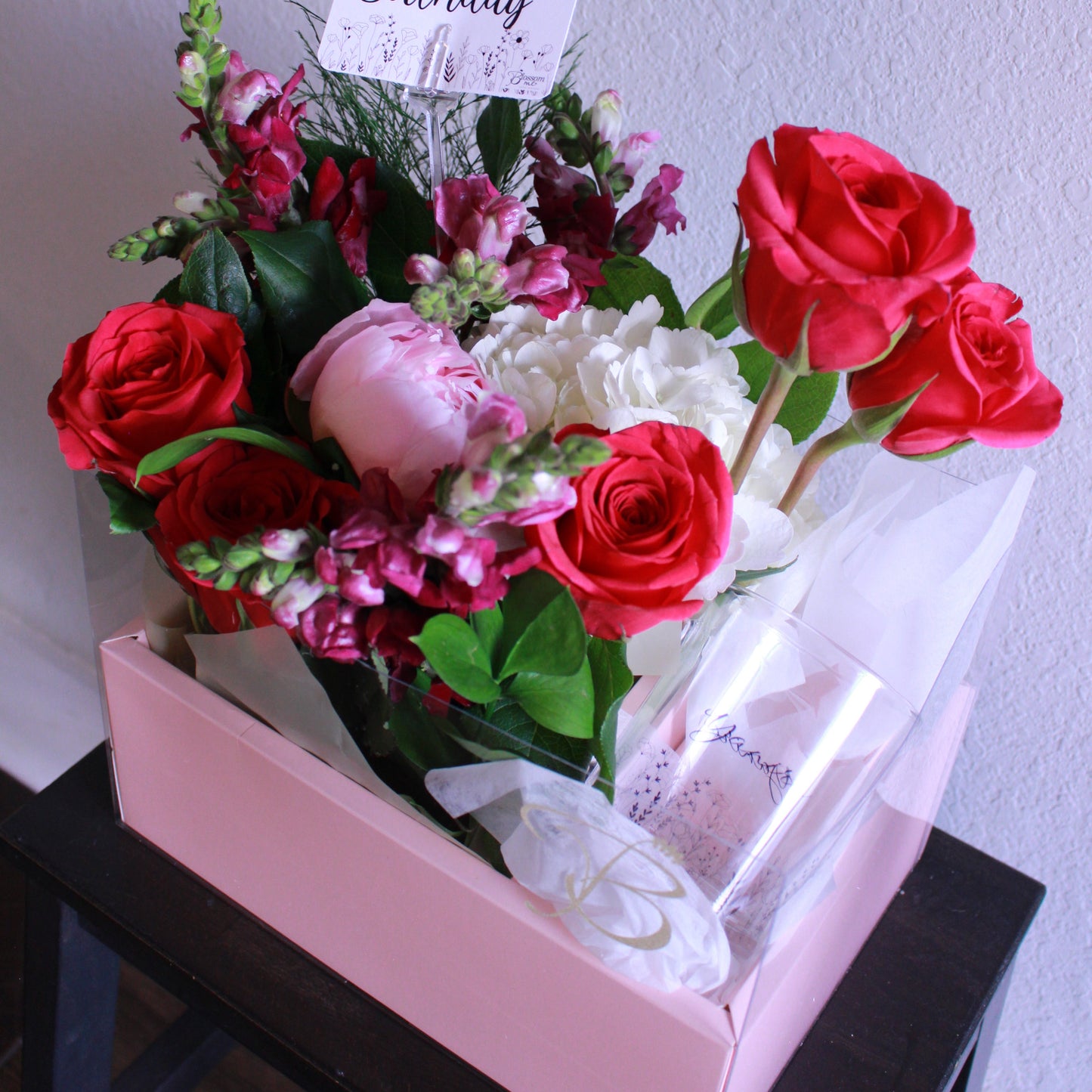 Bouquet of red and white roses with a 'Happy Birthday' card in a box on a light gray background